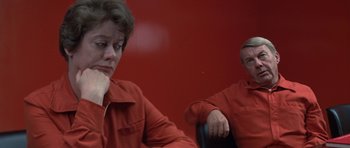 Movie still from “The Andromeda Strain” (1971), directed by Robert Wise – A woman in a red suit sitting next to a man in a red suit; Medium shot, Over the shoulder angle