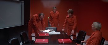 Movie still from “The Andromeda Strain” (1971), directed by Robert Wise – A group of people standing around a wooden table; Wide shot, High angle