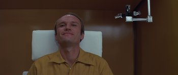 Movie still from “The Andromeda Strain” (1971), directed by Robert Wise – A man sitting in a chair looking up at the camera; Close Up shot, Low angle