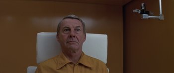 Movie still from “The Andromeda Strain” (1971), directed by Robert Wise – An older man wearing a yellow shirt sitting in a chair; Close Up shot, Low angle