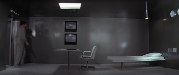 Movie still from “The Andromeda Strain” (1971), directed by Robert Wise – A room with a desk , chair and a television; Wide shot, High angle