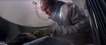 Movie still from “The Andromeda Strain” (1971), directed by Robert Wise – A man wearing a helmet and gloves looking down at something in his hand; Close Up shot, Low angle