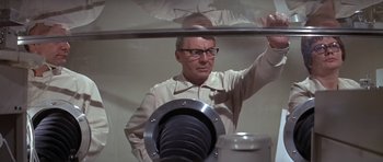 Movie still from “The Andromeda Strain” (1971), directed by Robert Wise – An older man in glasses and a white shirt is looking at the camera; Medium shot, Low angle