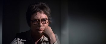 Movie still from “The Andromeda Strain” (1971), directed by Robert Wise – A woman with glasses is sitting with her hand on her chin; Close Up shot, Over the shoulder angle