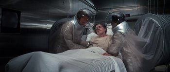 Movie still from “The Andromeda Strain” (1971), directed by Robert Wise – A man is in a hospital bed while two other men stand over him; Medium shot, High angle