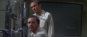 Movie still from “The Andromeda Strain” (1971), directed by Robert Wise – Two men standing next to each other in front of a window; Medium shot, Low angle
