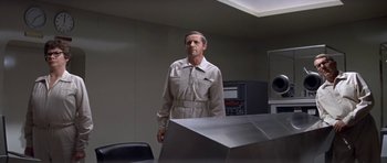 Movie still from “The Andromeda Strain” (1971), directed by Robert Wise – A man standing in front of a table in a room; Medium shot, Low angle