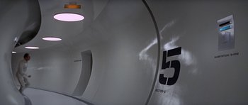 Movie still from “The Andromeda Strain” (1971), directed by Robert Wise – A white tunnel with numbers on the side of it; Extreme Wide shot, High angle