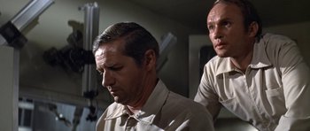 Movie still from “The Andromeda Strain” (1971), directed by Robert Wise – Two men in tan shirts and one is looking down at his face; Close Up shot, Low angle