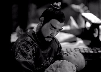 Movie still from “The Assassin” (2015), directed by Hsiao-Hsien Hou – A man holding a baby in his arms and wearing a crown; Medium shot, High angle