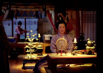 Movie still from “The Assassin” (2015), directed by Hsiao-Hsien Hou – A woman sitting at a table in a living room; Medium shot, Over the shoulder angle