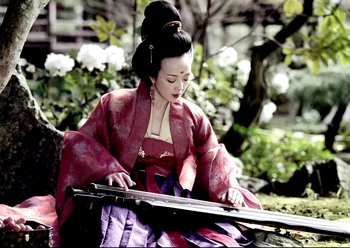 Movie still from “The Assassin” (2015), directed by Hsiao-Hsien Hou – A woman in a red and purple dress is playing an instrument; Medium shot, Low angle