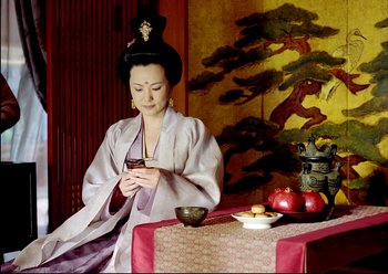 Movie still from “The Assassin” (2015), directed by Hsiao-Hsien Hou – A geisha is sitting at a table looking at her cell phone; Medium shot, Low angle