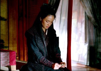 Movie still from “The Assassin” (2015), directed by Hsiao-Hsien Hou – A woman sitting on a chair looking at her cell phone; Medium shot, Over the shoulder angle