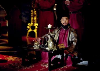 Movie still from “The Assassin” (2015), directed by Hsiao-Hsien Hou – A man sitting at a table in front of candles; Wide shot, High angle