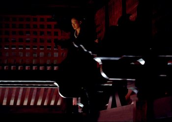Movie still from “The Assassin” (2015), directed by Hsiao-Hsien Hou – A woman sitting on a chair in a dark room; Wide shot, Low angle