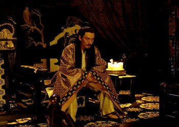 Movie still from “The Assassin” (2015), directed by Hsiao-Hsien Hou – A man sitting on a chair with a candle in front of him; Wide shot, High angle