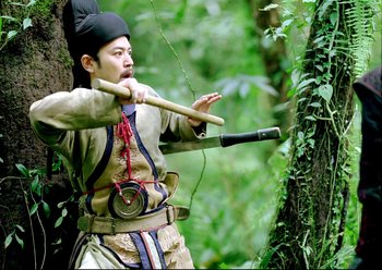 Movie still from “The Assassin” (2015), directed by Hsiao-Hsien Hou – A man holding a wooden stick in the woods; Medium shot, Low angle