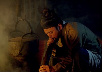 Movie still from “The Assassin” (2015), directed by Hsiao-Hsien Hou – A man is smoking a pipe in a dark room; Medium shot, Low angle