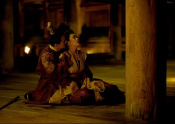 Movie still from “The Assassin” (2015), directed by Hsiao-Hsien Hou – A man and a woman sitting on the ground in front of a pillar; Medium shot, High angle