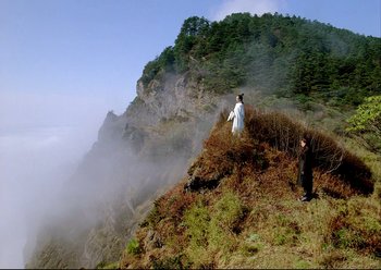 Movie still from “The Assassin” (2015), directed by Hsiao-Hsien Hou – Two people standing on a mountain side near a forest; Extreme Wide shot, Low angle