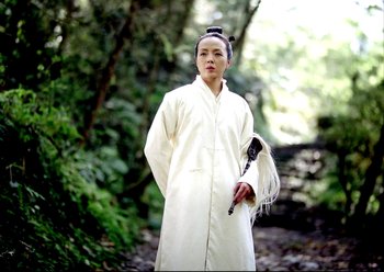 Movie still from “The Assassin” (2015), directed by Hsiao-Hsien Hou – A person in a white robe holding a stick in a forest; Medium shot, Low angle