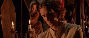Movie still from “The Baby of Mâcon” (1993), directed by Peter Greenaway – A man with long brown hair is looking at a candle; Close Up shot, Over the shoulder angle
