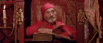 Movie still from “The Baby of Mâcon” (1993), directed by Peter Greenaway – An old man sitting at a table reading a book; Close Up shot, High angle