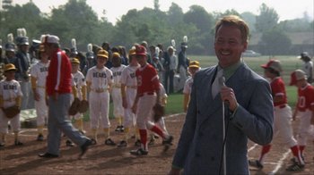 Movie still from “The Bad News Bears” (1976), directed by Michael Ritchie – A man in a baseball uniform is holding a microphone; Medium shot, Over the shoulder angle