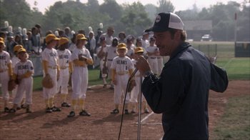 Movie still from “The Bad News Bears” (1976), directed by Michael Ritchie – A man holding a microphone in front of a group of young baseball players; Medium shot, Over the shoulder angle