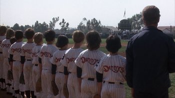 Movie still from “The Bad News Bears” (1976), directed by Michael Ritchie – A group of young baseball players lined up on a field; Wide shot, Over the shoulder angle