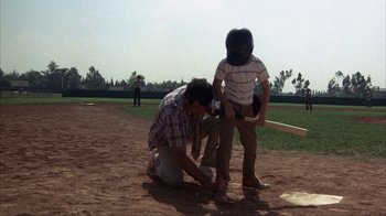 Movie still from “The Bad News Bears” (1976), directed by Michael Ritchie – A man kneeling down next to another man on a baseball field; Wide shot, High angle