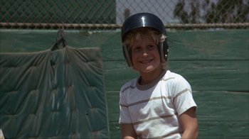 Movie still from “The Bad News Bears” (1976), directed by Michael Ritchie – A young boy wearing a baseball helmet and smiling for the camera; Medium shot, Low angle