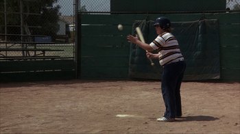 Movie still from “The Bad News Bears” (1976), directed by Michael Ritchie – A person swinging a baseball bat at a ball on a baseball field; Wide shot, High angle