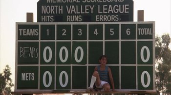 Movie still from “The Bad News Bears” (1976), directed by Michael Ritchie – A woman sitting on the ground in front of a baseball scoreboard; Wide shot, Low angle