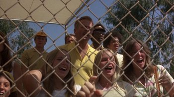 Movie still from “The Bad News Bears” (1976), directed by Michael Ritchie – A group of people standing behind a chain link fence; Medium shot, Low angle