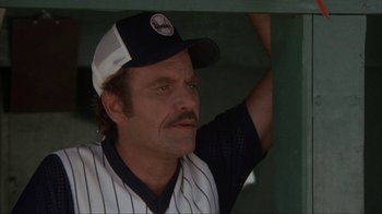 Movie still from “The Bad News Bears” (1976), directed by Michael Ritchie – A man in a baseball uniform and a hat is in a dugout; Close Up shot, Low angle