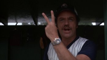 Movie still from “The Bad News Bears” (1976), directed by Michael Ritchie – A man in a baseball uniform making a peace sign with one hand; Close Up shot, Low angle