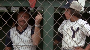 Movie still from “The Bad News Bears” (1976), directed by Michael Ritchie – Two baseball players are standing behind a fence; Medium shot, Over the shoulder angle
