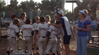 Movie still from “The Bad News Bears” (1976), directed by Michael Ritchie – A group of young baseball players gathered around a coach; Wide shot, Over the shoulder angle
