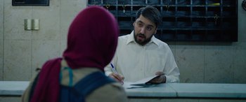 Movie still from “Holy Spider” (2022), directed by Ali Abbasi – A man in white shirt holding a pen and paper; Medium shot, Over the shoulder angle