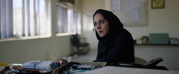 Movie still from “Holy Spider” (2022), directed by Ali Abbasi – A woman sitting at a table in a room; Close Up shot, Low angle