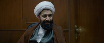 Movie still from “Holy Spider” (2022), directed by Ali Abbasi – A man with a beard is sitting in a chair and smoking a pipe; Close Up shot, Over the shoulder angle