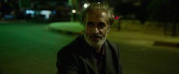 Movie still from “Holy Spider” (2022), directed by Ali Abbasi – A man in a suit and tie sitting on the street; Close Up shot, Over the shoulder angle