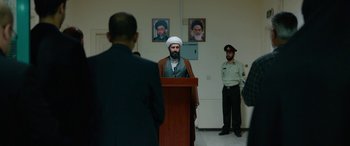 Movie still from “Holy Spider” (2022), directed by Ali Abbasi – A man is speaking in front of two other men; Wide shot, Over the shoulder angle