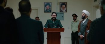 Movie still from “Holy Spider” (2022), directed by Ali Abbasi – A man in a military uniform is speaking at a podium; Medium shot, Over the shoulder angle
