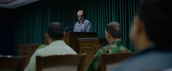 Movie still from “Holy Spider” (2022), directed by Ali Abbasi – A man standing at a podium in front of a group of people; Medium shot, Over the shoulder angle
