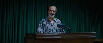 Movie still from “Holy Spider” (2022), directed by Ali Abbasi – A man standing at a podium with microphones in front of him; Medium shot, Over the shoulder angle