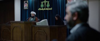 Movie still from “Holy Spider” (2022), directed by Ali Abbasi – A woman sitting in front of a judge in a courtroom; Wide shot, Over the shoulder angle