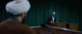 Movie still from “Holy Spider” (2022), directed by Ali Abbasi – A man standing at a podium speaking to a crowd; Medium shot, Over the shoulder angle